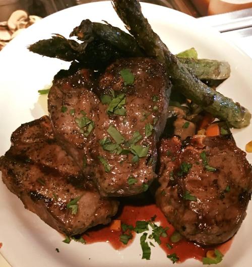 A plate of grilled steak with asparagus and colorful vegetables, garnished with fresh herbs.