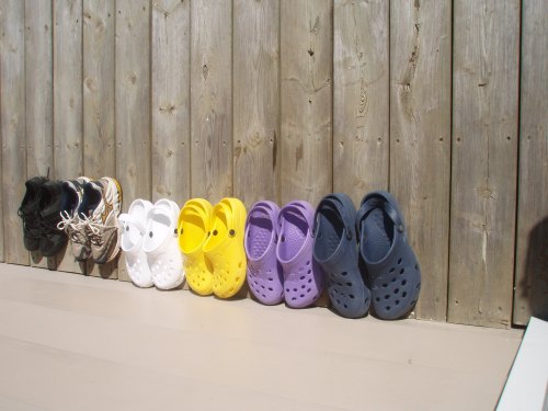 A row of colorful crocs and shoes lined up against a wooden fence.