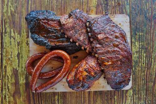 A wooden board displaying a variety of smoked meats, including ribs, brisket, and sausage.