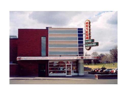 Exterior of a modern museum building with a retro sign, featuring large windows and a red brick facade.