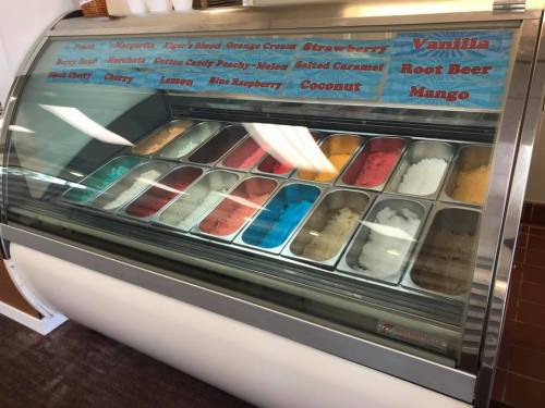 A display of colorful ice cream flavors in a glass case, including vanilla, strawberry, and mango.