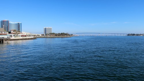A clear blue sky over a calm bay, with buildings and a bridge in the distance along the shoreline.