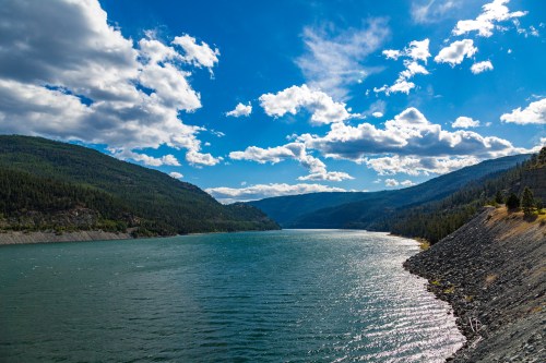 A serene lake surrounded by green mountains under a bright blue sky with fluffy clouds.