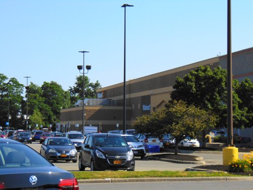 A busy parking lot with various cars in front of a large retail store on a sunny day.