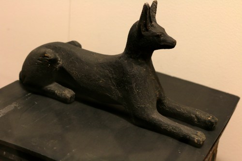 A black sculpture of a reclining dog, featuring pointed ears and a smooth, textured surface.