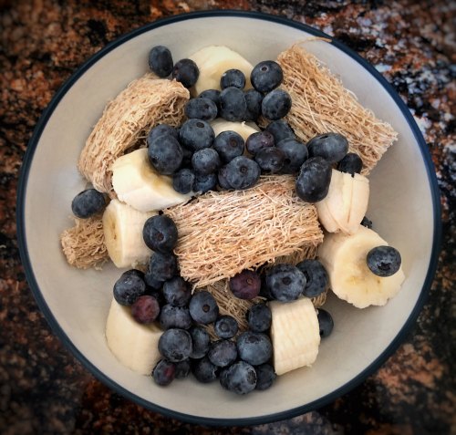 A bowl filled with shredded wheat, banana slices, and fresh blueberries on a textured surface.