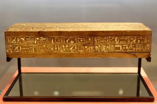 Ancient wooden artifact inscribed with Egyptian hieroglyphs, displayed on a stand.