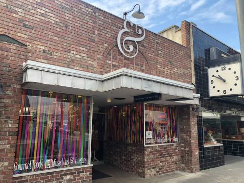 A brick storefront with colorful streamers in the windows, featuring a clock and signs for gourmet foods and gifts.