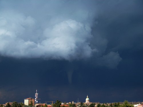A dark stormy sky with a funnel cloud descending towards the ground, set against a city skyline.