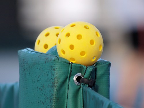 Two yellow pickleballs with holes resting on a green padded surface.