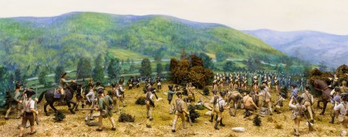 A detailed diorama depicting a historical battle scene with soldiers, trees, and rolling hills in the background.
