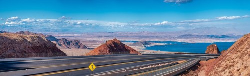 A scenic view of a winding road with mountains and a lake under a clear blue sky.