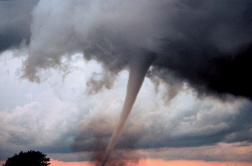 A tornado descends from dark storm clouds, creating a funnel shape against a dramatic sky.