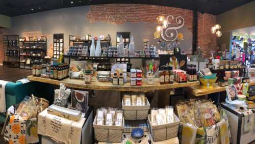 A cozy store interior featuring shelves of jars, kitchenware, and decorative items on a rustic wooden counter.