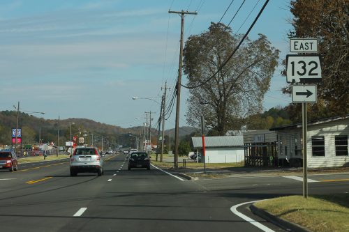 A road sign indicating Route 132 East, with cars and utility poles along a suburban street.