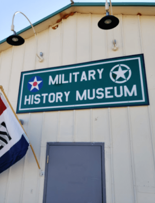 Sign for a Military History Museum on a building, with a flag in the foreground.
