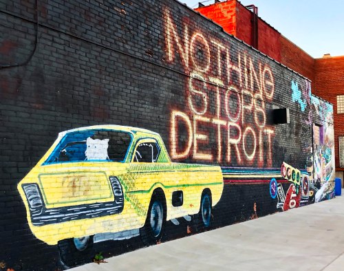 Colorful mural on a brick wall featuring a yellow car and the phrase "Nothing Stops Detroit."