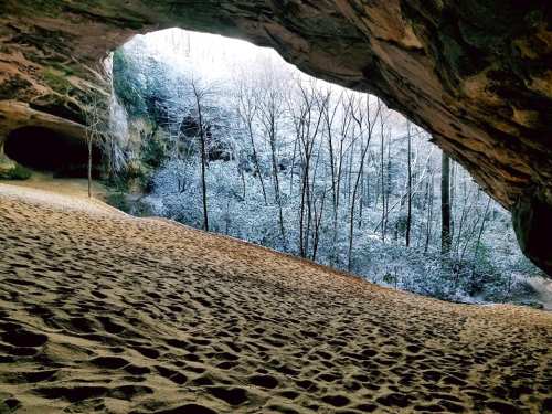 A sandy cave opening reveals a snowy forest landscape with bare trees in the background.