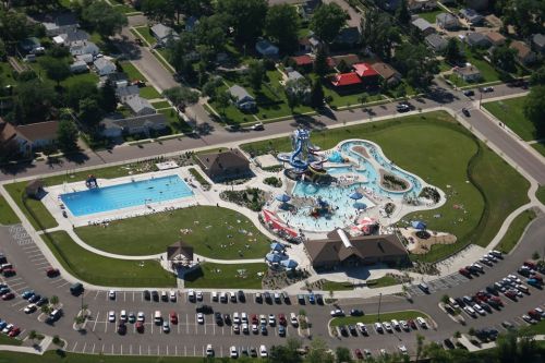 Aerial view of a water park featuring slides, a pool, and surrounding green areas with parked cars nearby.