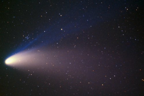 A bright comet with a glowing tail moves through a starry night sky, surrounded by countless stars.