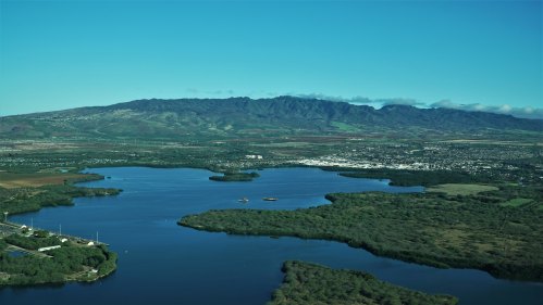 Aerial view of a lush landscape with a river, green vegetation, and mountains under a clear blue sky.