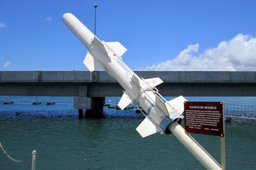 A Harpoon missile displayed near a bridge over calm waters, with a sign providing information about the missile.