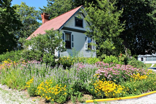 A charming house surrounded by vibrant flower beds in full bloom, featuring a mix of colorful blossoms and greenery.