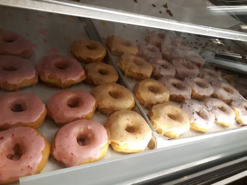 A display case filled with assorted donuts, featuring pink, cream, and chocolate-glazed varieties.