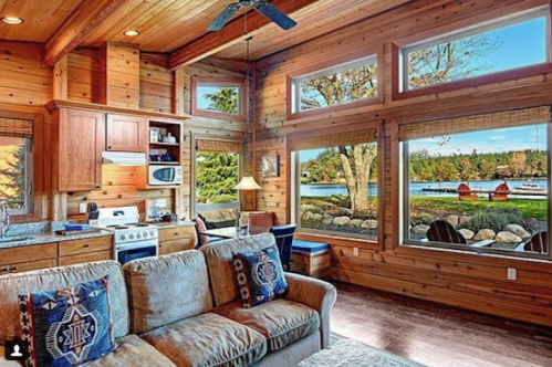 Cozy wooden cabin interior with a kitchen, living area, and large windows showcasing a scenic lake view.