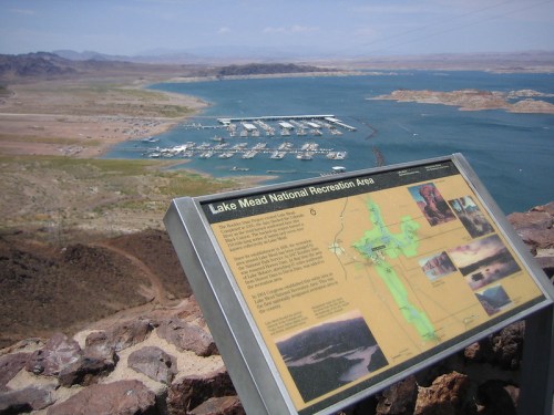 View of Lake Mead National Recreation Area with a marina and informational sign in the foreground. Clear blue skies above.