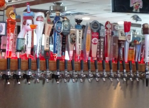 A row of colorful beer taps with various brands and styles displayed in a bar setting.