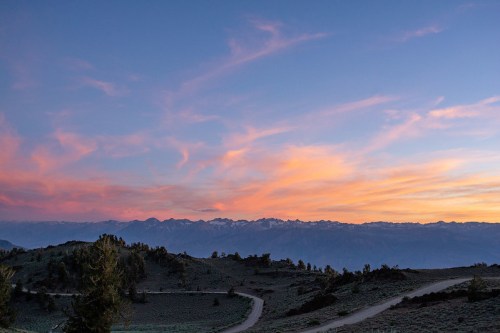 A serene sunset over mountains, with colorful clouds and a winding road in the foreground.