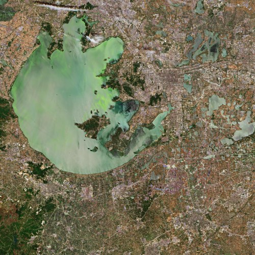 Aerial view of a large body of water surrounded by urban areas and greenery, showcasing a mix of land and water features.