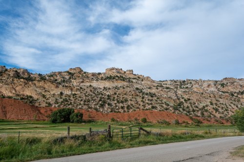 A scenic view of a rocky hillside with red and gray layers, set against a blue sky and green fields below.