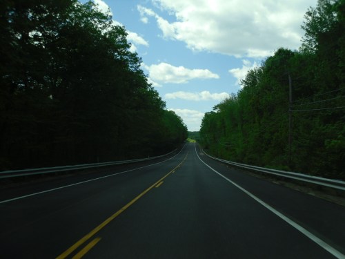 A winding road surrounded by lush green trees under a partly cloudy sky.