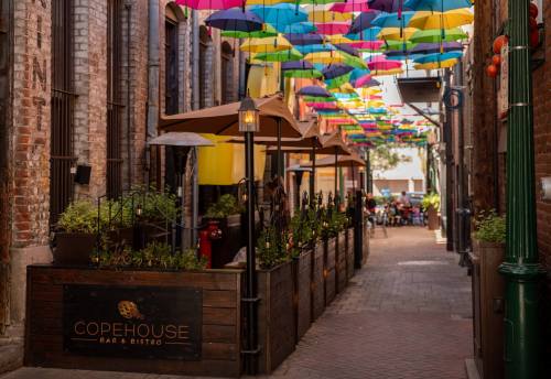 Colorful umbrellas hang above a charming alleyway with outdoor seating for Copehouse Bar and Bistro.