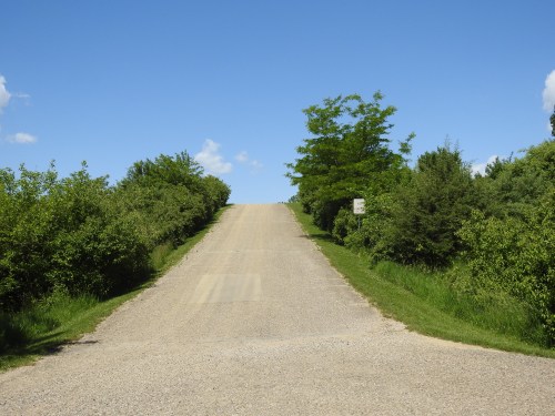A gravel road leads uphill, flanked by greenery under a clear blue sky.