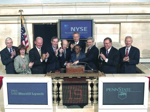 A group of people celebrating at the NYSE, marking an event on March 19, with banners for Merrill Lynch and Penn State.