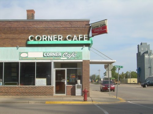 A brick building with a green awning and sign reading "Corner Cafe" at the intersection of Main Street.