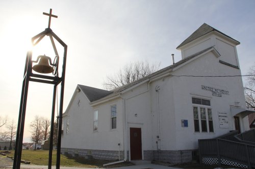 A white church building with a bell tower and cross, set against a bright sky.