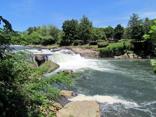 A scenic view of a waterfall surrounded by lush greenery and trees under a clear blue sky.