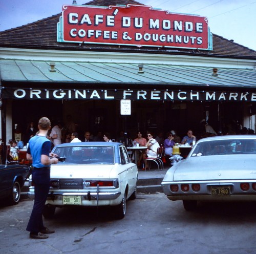 Café du Monde exterior with patrons enjoying coffee and doughnuts, vintage cars parked outside, in the French Market.