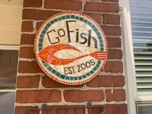Mosaic sign for "Go Fish," featuring a shrimp design and the text "EST. 2005," mounted on a brick wall.