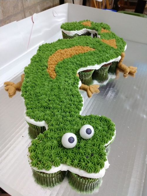 A large cupcake cake shaped like a green dragon, decorated with green frosting and big googly eyes.