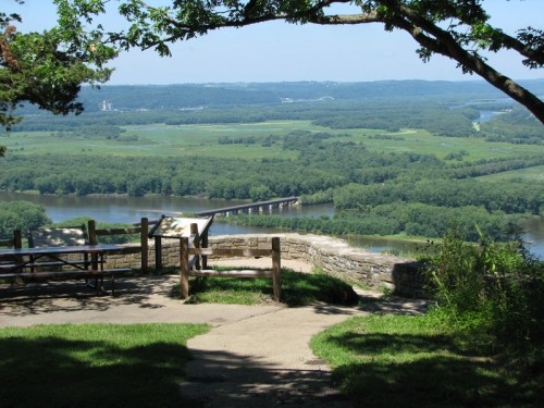 Scenic view from a lookout point overlooking a river and lush green landscape with a bridge in the distance.