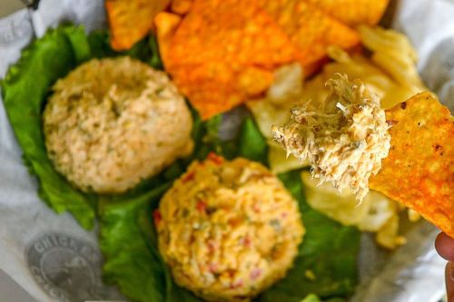Two scoops of chicken salad on lettuce, surrounded by tortilla chips and snacks. A chip is being dipped into the salad.
