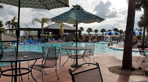 A pool area with umbrellas, lounge chairs, and palm trees under a cloudy sky, inviting relaxation and leisure.