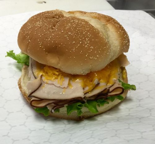 A sandwich with a sesame seed bun, layers of turkey, lettuce, and melted cheese.