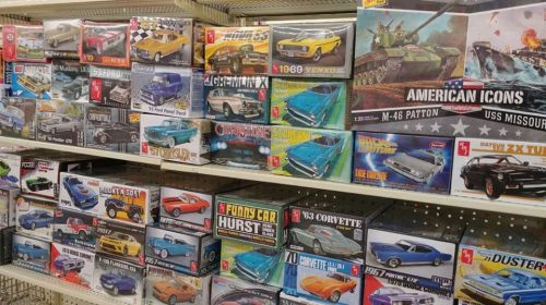 A display of various model kits, including cars and military vehicles, arranged on shelves in a store.