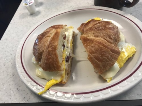 A croissant sandwich filled with eggs and cheese, cut in half, served on a white plate.
